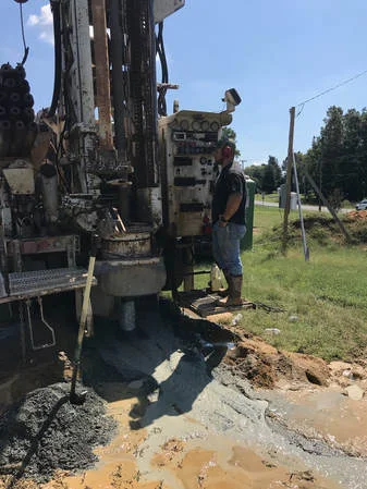 Dillon Wright, fourth-generation driller, at the rig controls with a pile of gray rock cuttings at the casing