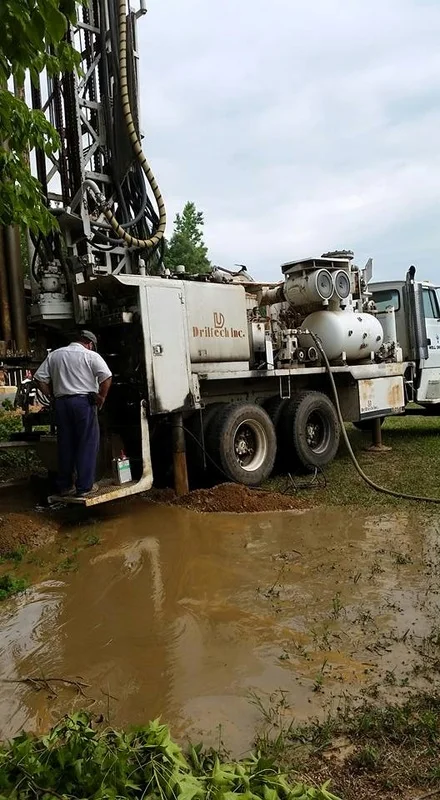 A Wright Well & Pump drill rig at work, with drilling water pooled in the red clay around it