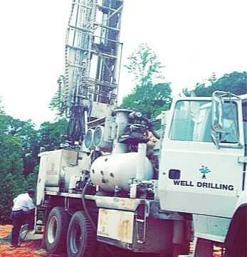 A white Wright drill rig, mast raised, its door lettered Well Drilling